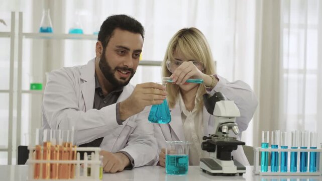 Male and female scientists and researchers in lab coats with microscope are conducting chemistry experiments with liquid in test tubes and beakers in laboratory. Two chemistry experts working in lab. 
