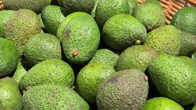 Close Up Look At Fresh Ripe Green Avocados In Wicker Basket Under Soft Supermarket Light
