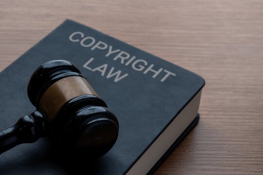 A black gavel and a book titled Copyright Law on a wooden desk. Intellectual property rights, legal protection, and the justice system concept.