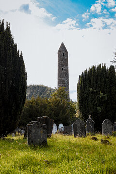 Ancient medieval round tower and historic cemetery headstones in Glendalough monastic site, County Wicklow, Ireland.