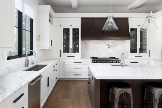 A kitchen detail with white cabinets, a large dark wood island with white marble countertop, and a brown metal range hood over a stainless steel stove.