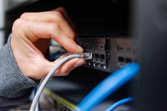 Close-up of a technician's hand plugging a grey ethernet network cable into a router or switch port.