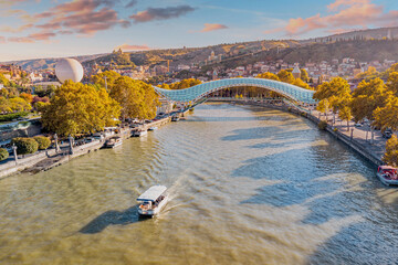 Aerial Tbilisi panorama featuring cruise boat and bridges spanning across Kura river © EdNurg