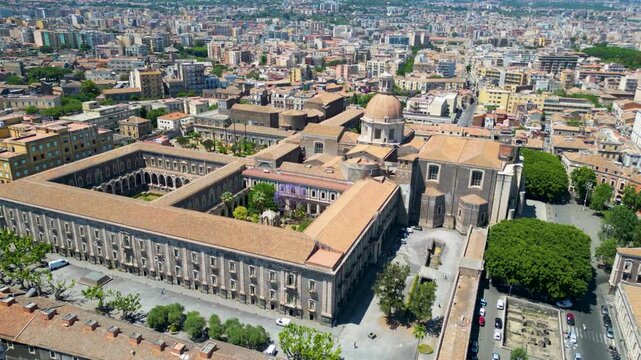 Aerial view of the historic Benedictine Monastery of San Nicolo l'Arena with its large courtyard and dome amidst the urban landscape of Catania, Sicily, Italy.