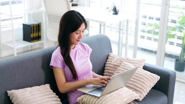 Smiling young woman working on laptop in living room, checking email in morning, writing message in social network, happy young female using internet banking service, searching information.