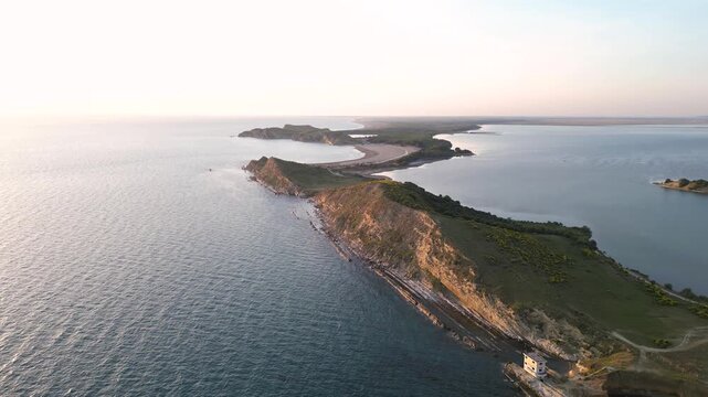 Aerial view of the Zvernec peninsula featuring rocky cliffs and lush green vegetation surrounded by the calm waters of the Adriatic Sea in Zvernec, Vlore County, Albania.