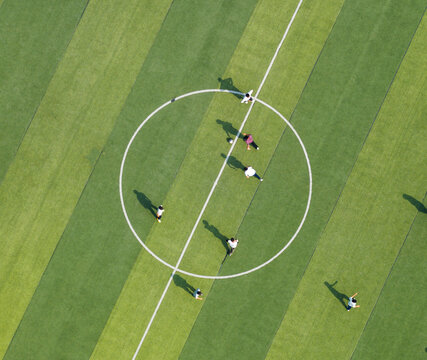 Aerial view of students playing soccer on a green campus field. Promoting physical education and teamwork during break time. Vibrant school sports scene.	
