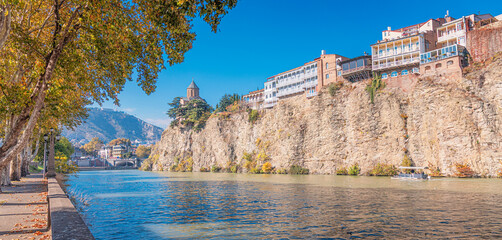 Mtkvari river flowing past ancient churches and traditional buildings built on a rocky cliff in Tbilisi historic district, Georgia © EdNurg