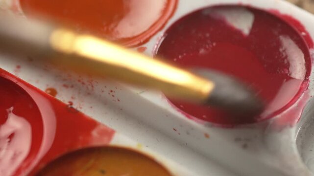 A man dips a brush into red paint for his crative hobby, creative process, and relaxing art therapy session.