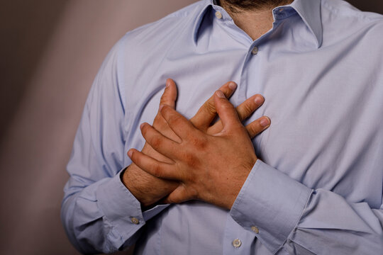 Close up of a man in a blue shirt clutching his chest in distress.