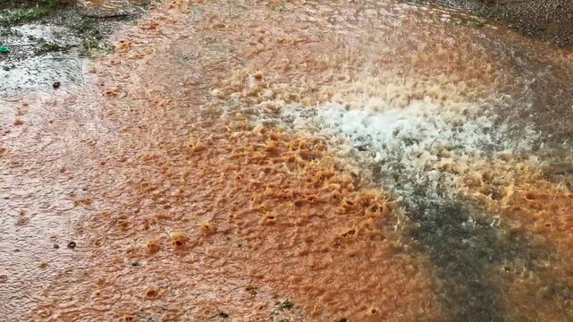 Heavy rainfall striking the ground and creating splashes on a wet surface, capturing the intensity and atmosphere of a monsoon downpour