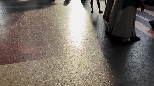 Close-up of traditionally dressed Indian people walking across a sunlit floor, with moving feet and sharp shadows creating dynamic patterns during a cultural gathering or festival