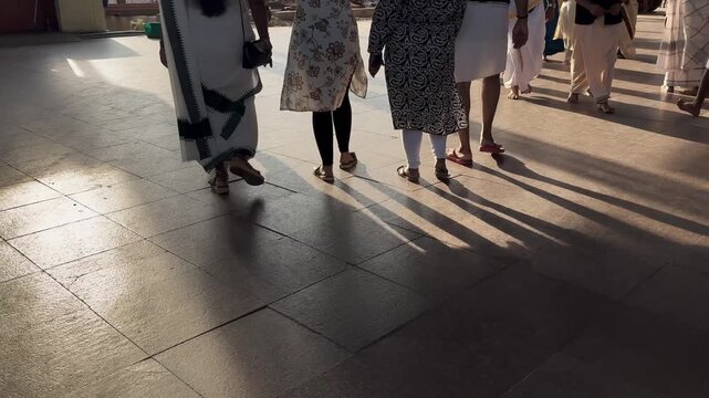 Close-up of traditionally dressed Indian people walking across a sunlit floor, with moving feet and sharp shadows creating dynamic patterns during a cultural gathering or festival