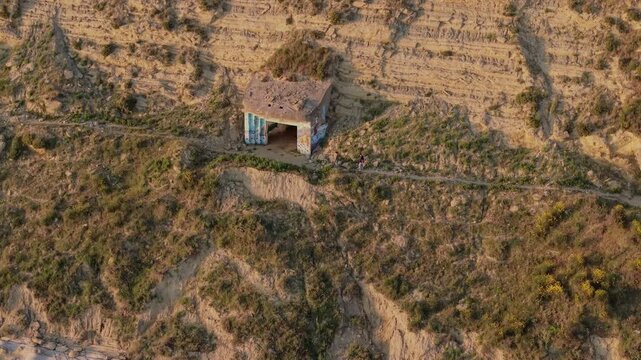 Aerial view of an abandoned concrete bunker on a dry hillside with two people walking along a path in Vjose - Narte Delta Protected Area, Zvernec, Vlore County, Albania.