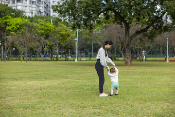 Fototapeta premium Mother watching her little toddler walk on grass