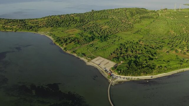 Aerial view of the wooden bridge leading to Zvernec Island within the Vjose-Narte Delta Protected Area with lush green hills and calm lagoon waters in Zvernec, Vlore County, Albania.
