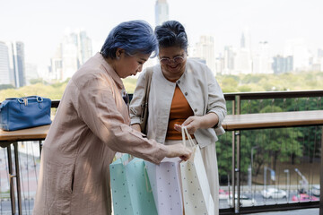 Obraz premium Two senior Asian women check their shopping bags together on a city, highlighting retail leisure, friendship and active aging lifestyle. reflecting friendship, active aging, and social connection