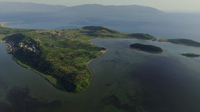 Aerial view of the Vjose-Narte Delta Protected Area featuring the Zvernec lagoon and lush green hills under a clear sky in Zvernec, Vlore County, Albania.