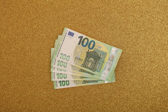Close up of multiple one hundred euro bills fanned out on a shimmering golden surface.