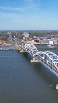 Aerial view of the white arched Merwedebrug crossing the river with heavy traffic and industrial buildings under a clear blue sky in Gorinchem, South Holland, Netherlands.