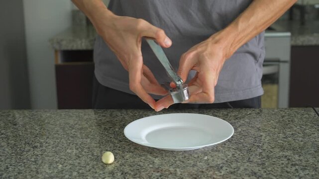 Close up man crushing garlic with garlic press with clear sound. Hands squeezing cloves in kitchen tool. Cooking preparation, fresh ingredients, kitchen routine and ASMR concept.