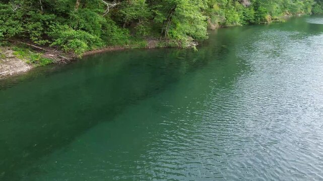 Hovering over a clear river in the Pacific Northwest, on a late spring morning the camera pans right showing up river views of a gravel bar at the bottom of redwood covered hills.