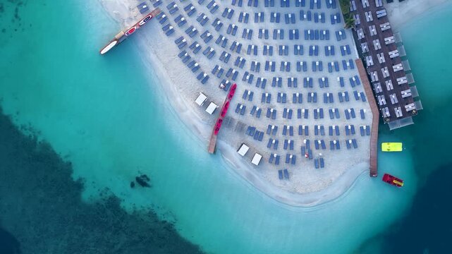 Aerial view of rows of blue sun loungers on a white sand beach with turquoise water and wooden docks in Ksamil, Vlore County, Albania.