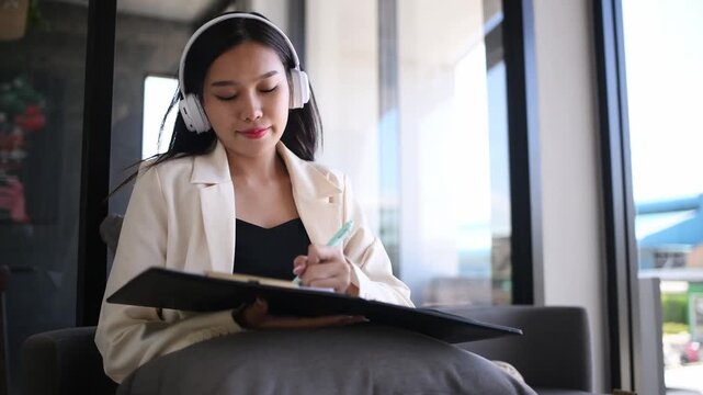 Businesswoman sitting indoor space wearing headphones while writing notes focused and productive work in a relaxed environment concepts of business education productivity and online learning.