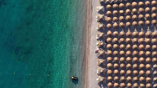 Aerial view of Llamani Beach featuring rows of straw umbrellas and turquoise water on the coastline in Himare, Vlore County, Albania.