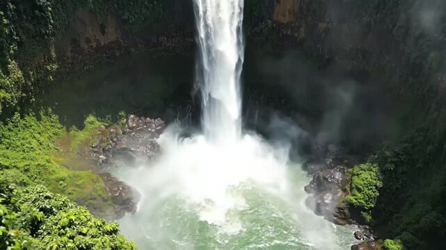 Waterfall cascading into lush tropical rainforest canyon with ferns