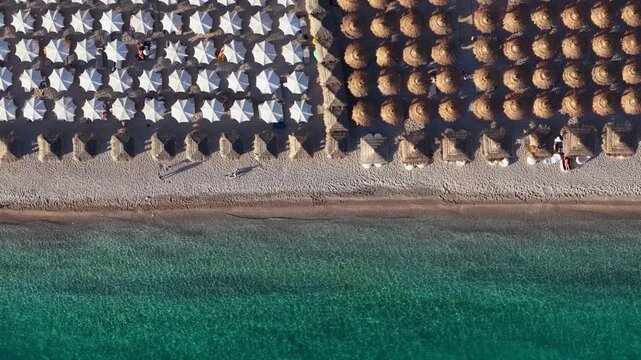 Aerial view of Llamani Beach featuring rows of white and straw umbrellas on the shore with turquoise sea water in Himare, Vlore County, Albania.