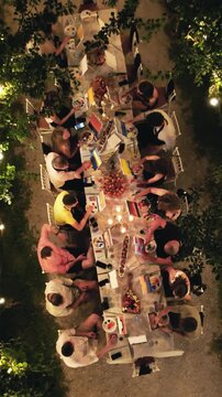 People at outdoor evening gathering painting on canvas under string lights and trees with a festive ambiance