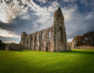 ruins of a stone abbey stand in a green field under a cloudy sky evocative of history
