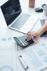 Accounting and Financial Analysis: A person's hands meticulously work a calculator, surrounded by financial reports, charts, and a laptop. © Kritdanai
