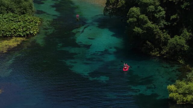 Aerial view of people in a red boat on the crystal clear turquoise waters of the Blue Eye spring surrounded by lush green forest in Finiq, Vlore County, Albania.