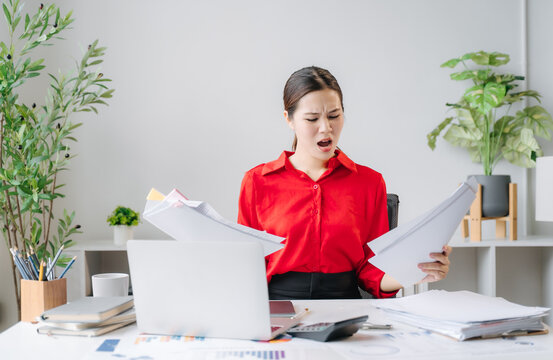 Overwhelmed Employee at Desk: A frustrated female office worker sits at a cluttered desk, overwhelmed by paperwork and bills, with a stressed expression.