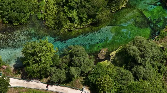 Aerial view of the Blue Eye spring with crystal clear turquoise water surrounded by dense green forest in Finiq, Vlore County, Albania.