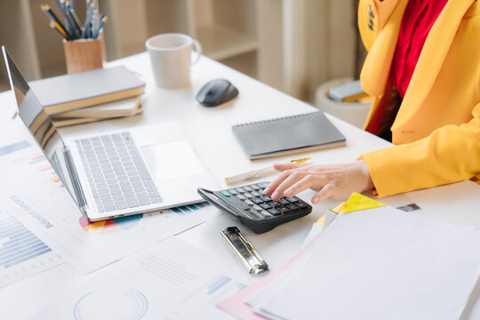 Busy Desk, Focused Mind: A professional works diligently at a desk, surrounded by reports and a laptop, using a calculator to manage finances.
