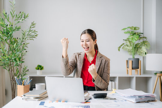 Successful Businesswoman Celebrating at Desk: A young businesswoman in a smart suit expresses elation at her desk.