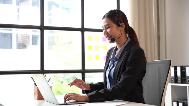 Professional Consultation: A smiling female customer service representative with a headset and a business suit is actively engaged in a conversation on her laptop.
