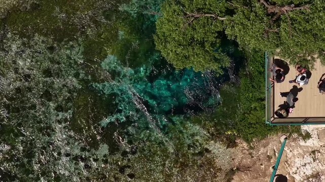 Aerial view of the Blue Eye natural spring with crystal clear turquoise water and tourists on a viewing platform in Finiq, Vlore County, Albania.