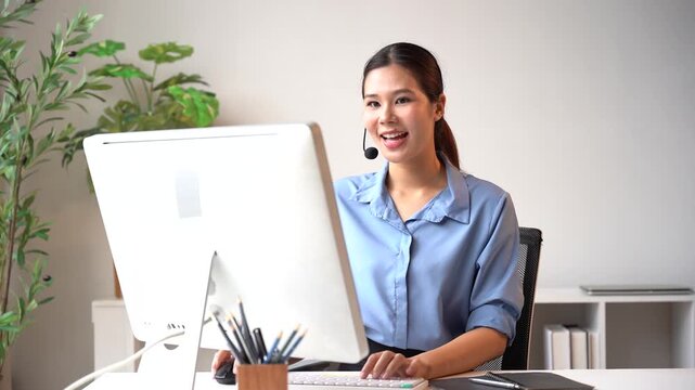 Customer Support Operator Smiling at Computer: A cheerful female customer support operator wearing a headset smiles while working at her computer.