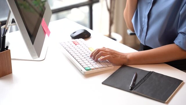 Office Worker Typing on Keyboard: A close-up shot of a person's hands typing on a keyboard of a computer in an office setting, showcasing productivity and focus.