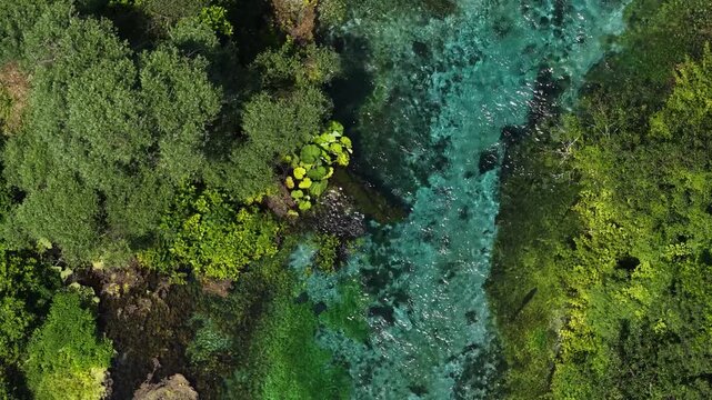 Aerial view of the crystal clear turquoise waters of the Blue Eye spring surrounded by lush green forest in Finiq, Vlore County, Albania.