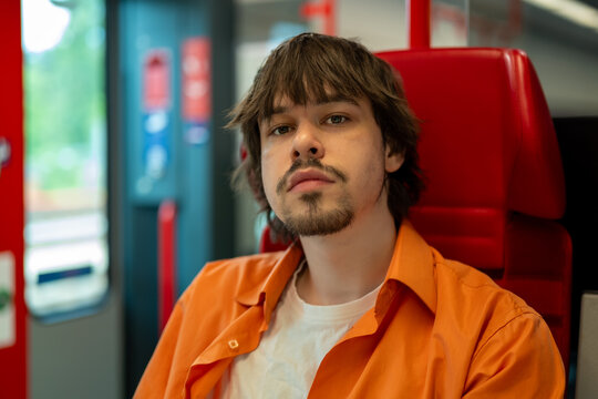 Young man sits in a modern train and looks at the camera.