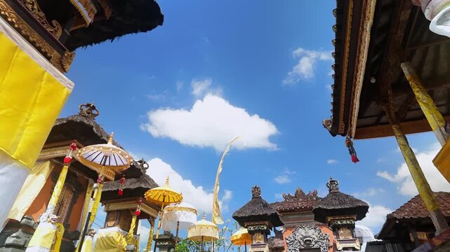 Low angle time lapse of a Balinese Hindu temple courtyard adorned with ceremonial umbrellas against a blue sky