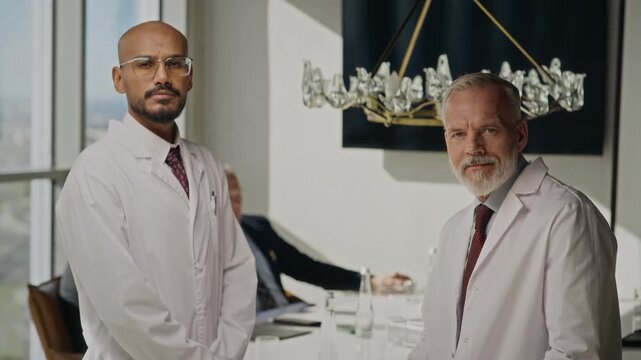 Portrait of middle aged Caucasian scientist and young adult Indian engineer in lab coats looking at clipboard then turning to camera. Perfect for energy sector corporate videos and RD promos