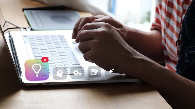 Asian man typing on laptop keyboard at his desk, where a 3D tracked bright lightbulb badge, human head gear charts, and virtual brain infographics appear.