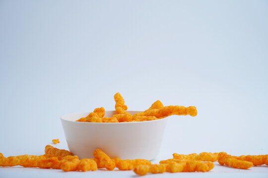 Crispy cheese corn roll snack or cheese corn puff in a white plastic bowl with some beside the bowl. Isolated White snack concept