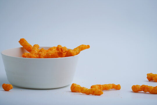 closeup Crispy cheese roll corn snack in a white plastic bowl or cheese puffcorn scattered beside it isolated on a white background